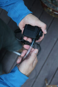 man holding a black water pump with clear plastic tubing attached